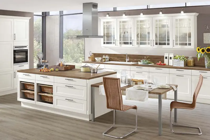 Klassische Landhausküche in Weiß mit Kochinsel, Glasfronten und Holzarbeitsplatte. Einbauküche im Landhausstil mit gemütlicher Atmosphäre und viel Stauraum.